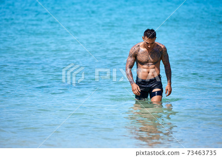 Athletic young tattooed guy at the beach 73463735