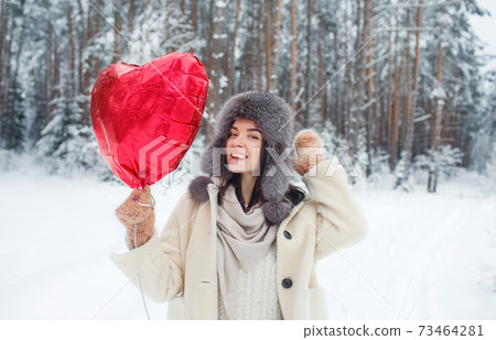 Portrait of a young girl with a bright heart-shaped balloon in a snow-covered forest. Valentine's Day Portrait of a young girl with a bright heart-shaped balloon in a snow-covered forest. Valentine's Day 73464281