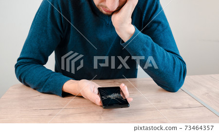 unhappy young man looking at his smartphone with a broken screen. 73464357