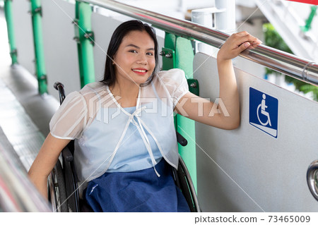 Young disabled woman in wheelchair near handicapped walkway sign, transportation convenience for disabled people concept. 73465009