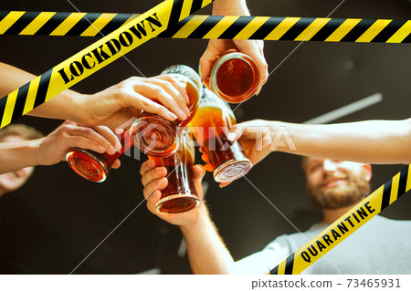 Close up hands clinking glasses of beer at bar with bounding tapes Lockdown, Coronavirus, Quarantine, Warning - closing bars and nightclubs during pandemic Close up hands clinking glasses of beer at bar with bounding tapes Lockdown, Coronavirus, Quarantine, Warning - closing bars and nightclubs during pandemic 73465931