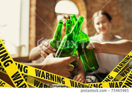 Close up hands clinking bottles of beer at bar with bounding tapes Lockdown, Coronavirus, Quarantine, Warning - closing bars and nightclubs during pandemic Close up hands clinking bottles of beer at bar with bounding tapes Lockdown, Coronavirus, Quarantine, Warning - closing bars and nightclubs during pandemic 73465965
