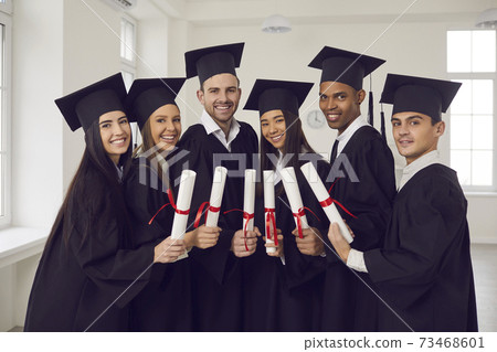 Group of happy multiethnic university graduates in black mantles standing with diplomas in hands Group of happy multiethnic university graduates in black mantles standing with diplomas in hands 73468601