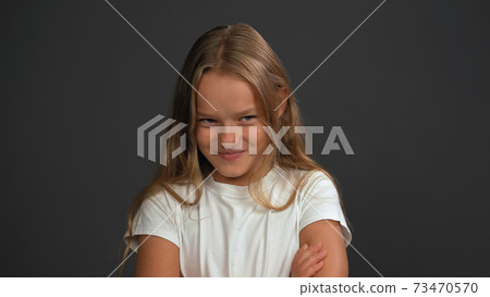 Close up. Little girl of 8,10 years with hands folded looks looks questioningly at the camera wearing white t shirt isolated on dark grey or black background Close up. Little girl of 8,10 years with hands folded looks looks questioningly at the camera wearing white t shirt isolated on dark grey or black background 73470570