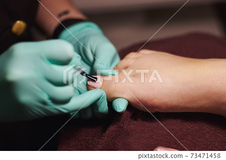 Pedicurist's hands in green medical gloves doing pedicure in professional beauty salon. Body care. Pedicurist's hands in green medical gloves doing pedicure in professional beauty salon. Body care. 73471458