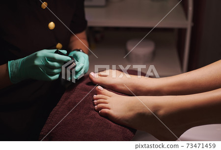 Young woman getting professional pedicure in beauty salon. Cropped view of pedicurist's hands and woman legs Young woman getting professional pedicure in beauty salon. Cropped view of pedicurist's hands and woman legs 73471459