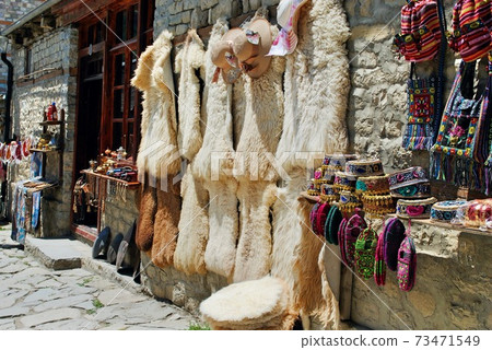 A display of traditional Azeri souvenir hats, bags, knitted socks and sheepskin furs on the Main Street of Lahic, a highland village in Azerbaijan. 73471549