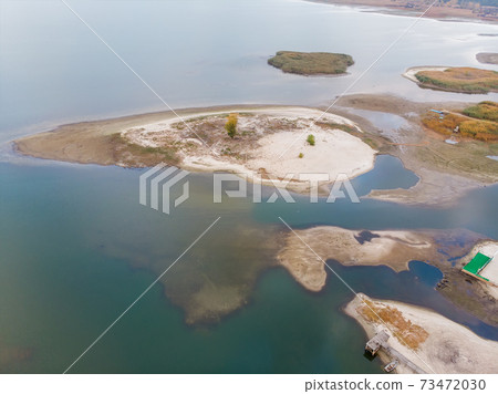 Scenic aerial drone birds eye view of swallow sand river or lake shore due to drought and water pond reservoir dam draining. Natural disaster of arid, warmand dry climate change Scenic aerial drone birds eye view of swallow sand river or lake shore due to drought and water pond reservoir dam draining. Natural disaster of arid, warmand dry climate change 73472030