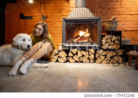 Woman by the fireplace with a white dog Woman by the fireplace with a white dog 73472286