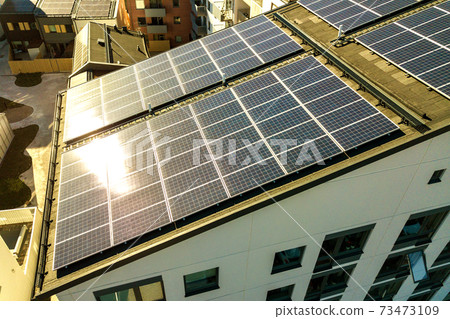 Aerial view of solar photovoltaic panels on a roof top of residential building block for producing clean electric energy. Autonomous housing concept. Aerial view of solar photovoltaic panels on a roof top of residential building block for producing clean electric energy. Autonomous housing concept. 73473109