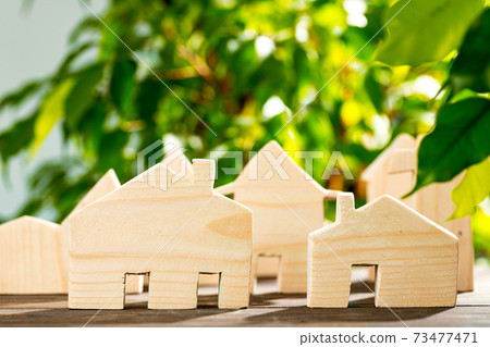 Toy wooden house on wooden table against foliage background Toy wooden house on wooden table against foliage background 73477471