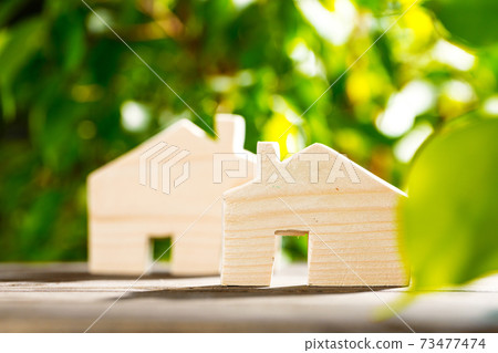 Toy wooden house on wooden table against foliage background Toy wooden house on wooden table against foliage background 73477474
