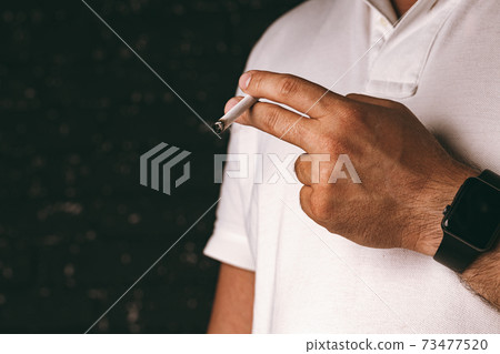 Male hand holding lit cigarette against black background Male hand holding lit cigarette against black background 73477520