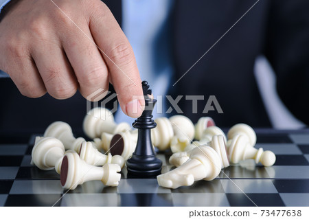 Businessman finger hands control chess king to success position on competition business game with falling enemy chess, meaning of planning and strategy decision and achievement goal concept. Businessman finger hands control chess king to success position on competition business game with falling enemy chess, meaning of planning and strategy decision and achievement goal concept. 73477638