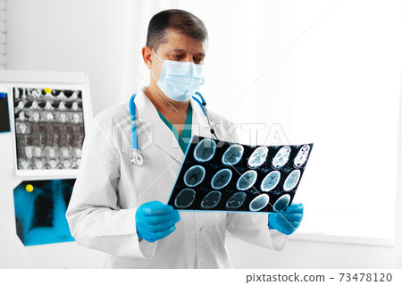 Senior man doctor in mask examines head MRI in hospital 73478120