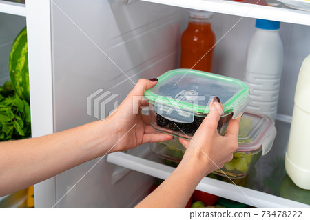 Female hands taking storage box with food from a fridge Female hands taking storage box with food from a fridge 73478222