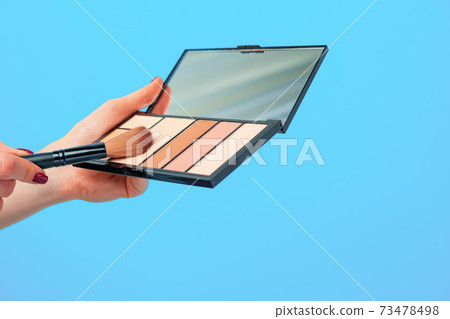 Female hand holding cosmetic palette against blue background 73478498