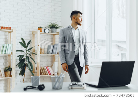 Young businessman standing by the window at his office 73478505