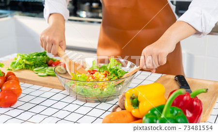woman in the process of preparing healthy food Vegetable Salad mixing salad wooden spoon in kitchen at home Dieting Concept woman in the process of preparing healthy food Vegetable Salad mixing salad wooden spoon in kitchen at home Dieting Concept 73481554