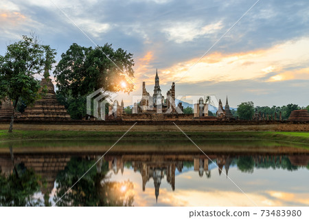Buddha statue and pagoda Wat Mahathat temple with reflection during sun set, Sukhothai Historical Park, Thailand 73483980