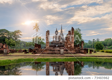 Buddha statue and pagoda Wat Mahathat temple with reflection during sun set, Sukhothai Historical Park, Thailand 73483982