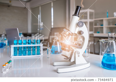 Microscope examining slide of sample with test tubes in background. Concept for science and technology research in laboratory. Microscope examining slide of sample with test tubes in background. Concept for science and technology research in laboratory. 73484971