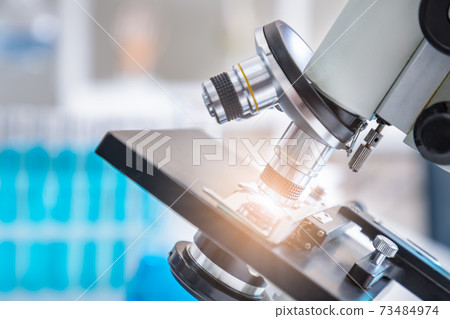 Close-up of microscope examining slide of sample with test tubes in background. Concept for science and technology research in laboratory. Close-up of microscope examining slide of sample with test tubes in background. Concept for science and technology research in laboratory. 73484974