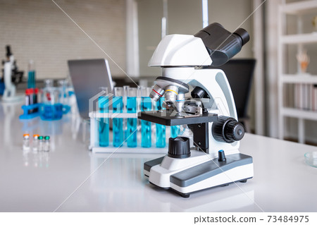 Microscope examining slide of sample with test tubes in background. Concept for science and technology research in laboratory. Microscope examining slide of sample with test tubes in background. Concept for science and technology research in laboratory. 73484975