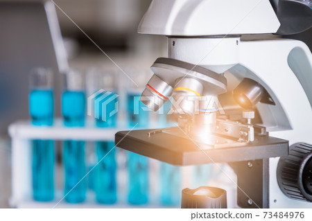 Close-up of microscope examining slide of sample with test tubes in background. Concept for science and technology research in laboratory. Close-up of microscope examining slide of sample with test tubes in background. Concept for science and technology research in laboratory. 73484976
