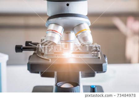 Close-up of microscope examining slide of sample. Concept for science and technology research in laboratory. Close-up of microscope examining slide of sample. Concept for science and technology research in laboratory. 73484978