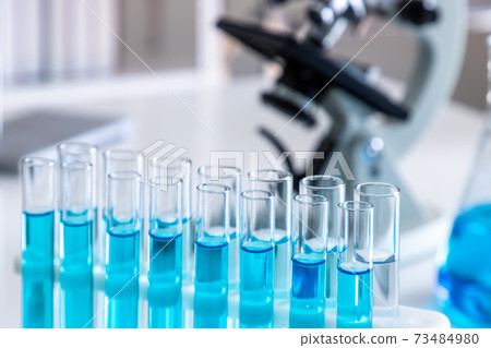 Test tubes with blue liquid in holder with microscope in background. Science glass equipment in laboratory for chemistry and medical research. Test tubes with blue liquid in holder with microscope in background. Science glass equipment in laboratory for chemistry and medical research. 73484980
