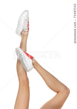 Close-up shapely female legs in white footwear isolated over studio background 73485543