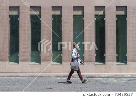 Young businessman walking next to office buildings while holding a shoulder bag outdoors Young businessman walking next to office buildings while holding a shoulder bag outdoors 73489537
