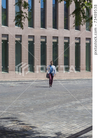 Young businessman walking next to office buildings while holding a shoulder bag outdoors Young businessman walking next to office buildings while holding a shoulder bag outdoors 73489538