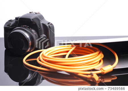 Digital photo camera connected to laptop with orange rolled cable Digital photo camera connected to laptop with orange rolled cable 73489566
