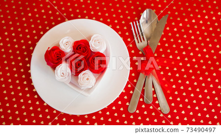 A white plate with a knife and fork on a bright red background 73490497