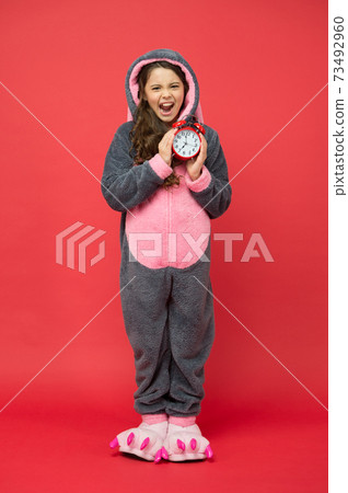 Early rise. angry kid in kigurumi pajama hold alarm clock. Early rise. angry kid in kigurumi pajama hold alarm clock. 73492960