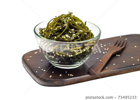 Seaweed kelp (Laminaria) in a glass bowl, sprinkle sesame seeds on a wooden board, Isolate on white background. Seaweed salad. Healthy food concept. Seaweed kelp (Laminaria) in a glass bowl, sprinkle sesame seeds on a wooden board, Isolate on white background. Seaweed salad. Healthy food concept. 73495233