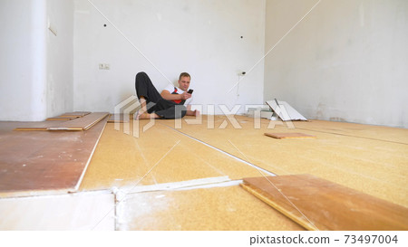 Builder in renovated room lying on floor using smartphone Builder in renovated room lying on floor using smartphone 73497004