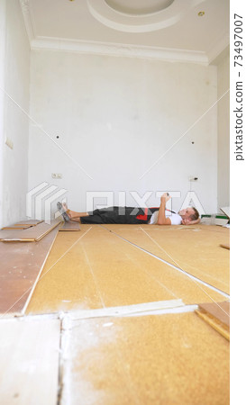 Builder in renovated room lying on floor using smartphone 73497007
