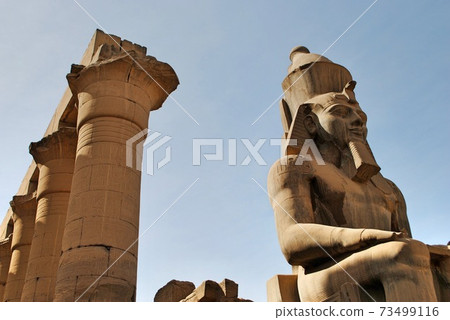 Colossus of Pharaoh Ramses II sitting in front to tall columns on throne carved with ancient Egyptian hieroglyphics, Luxor Temple. Luxor Egypt. UNESCO World Heritage Site. Colossus of Pharaoh Ramses II sitting in front to tall columns on throne carved with ancient Egyptian hieroglyphics, Luxor Temple. Luxor Egypt. UNESCO World Heritage Site. 73499116