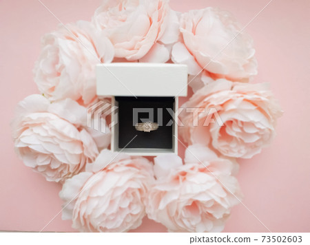 In the jewelry box there is a ring in a frame of pink delicate peonies on a beautiful pink background. Romantic concept. Flat style. In the jewelry box there is a ring in a frame of pink delicate peonies on a beautiful pink background. Romantic concept. Flat style. 73502603