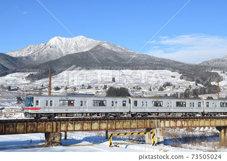 Nagano Electric Railway 3000 series train crossing Yomasebashi with the snowy mountains of Kita-Shiga in the background 73505024