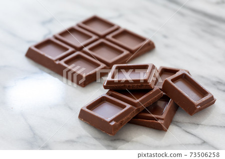 Broken chocolate bar on a marble table 73506258