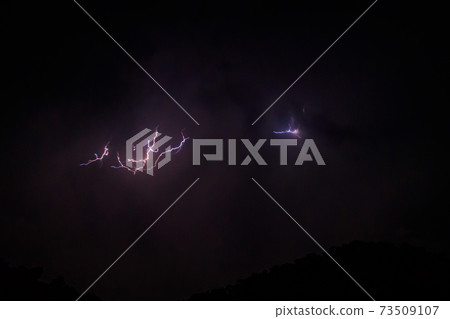 Lightning discharges in the stormy sky under dark rain clouds at night 73509107