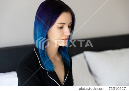 Beautiful woman with blue hair in black nightwear sitting on bed after sleep 73510627