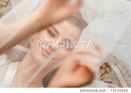 view top. a beautiful young woman is lying under a veil. hands over face. 73510850