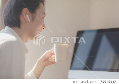 A young man working on a computer while looking at coffee A young man working on a computer while looking at coffee 73515342
