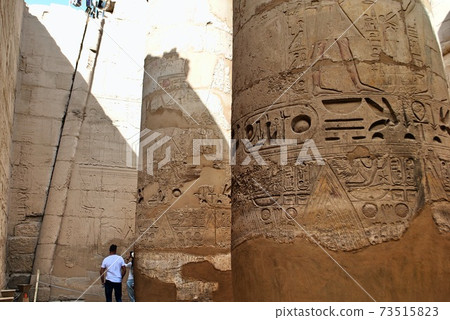 Tourists try to read the ancient Egyptian hieroglyphs carved on huge stone columns at Karnak Temple. Luxor Egypt. Unesco World Heritage Site.  73515823