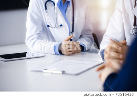 Two doctors and patient woman discussing something while sitting at the desk in modern clinic. Perfect medical service, medicine concept 73516436